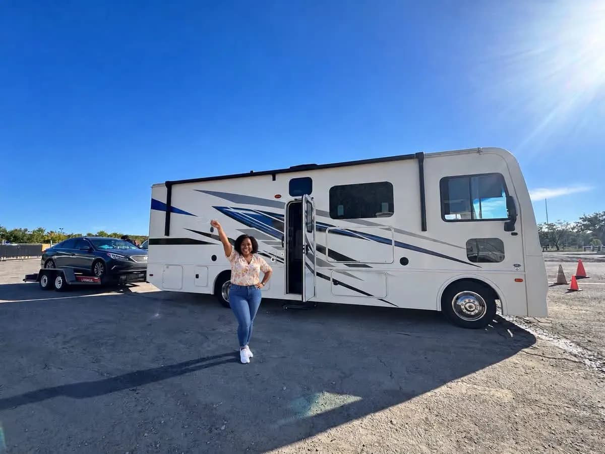 Customer raising her keys beside a Class A motorhome with her car on a tow dolly