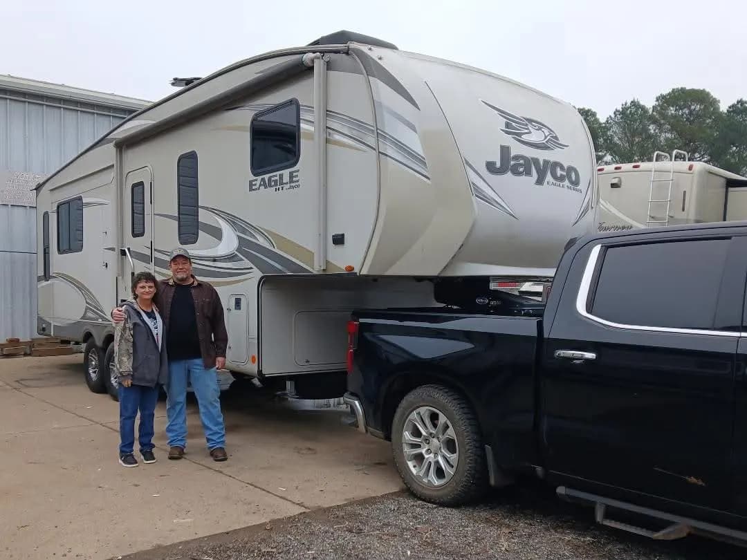 Couple beside their Jayco Eagle HT fifth wheel, hitched to their pickup truck